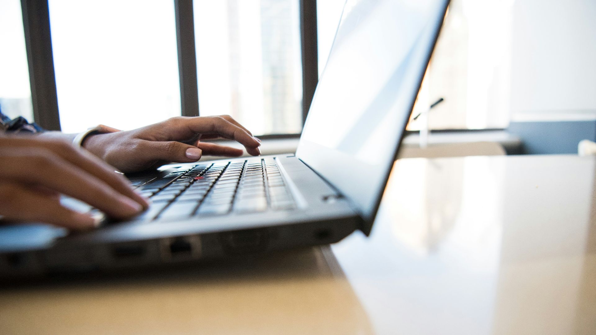 person using black laptop on brown table