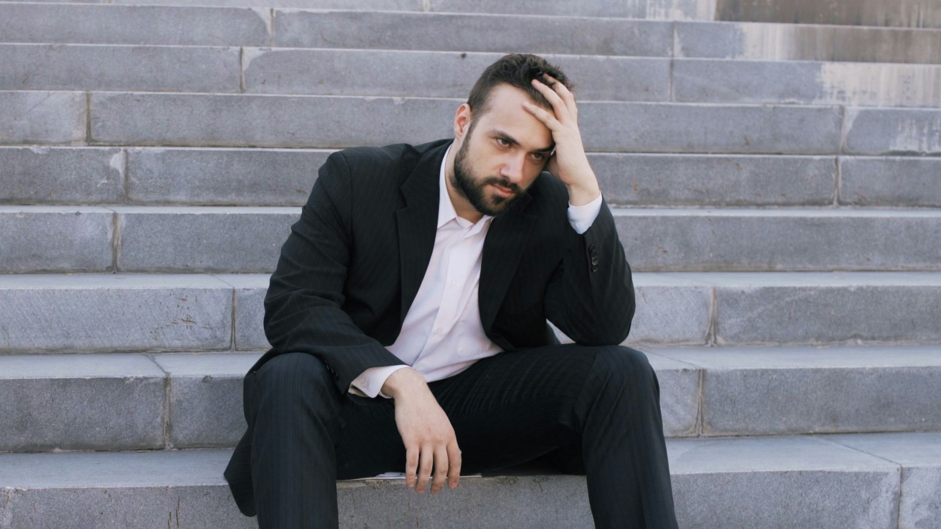 Man in suit sitting on outdoor stairs looking down.