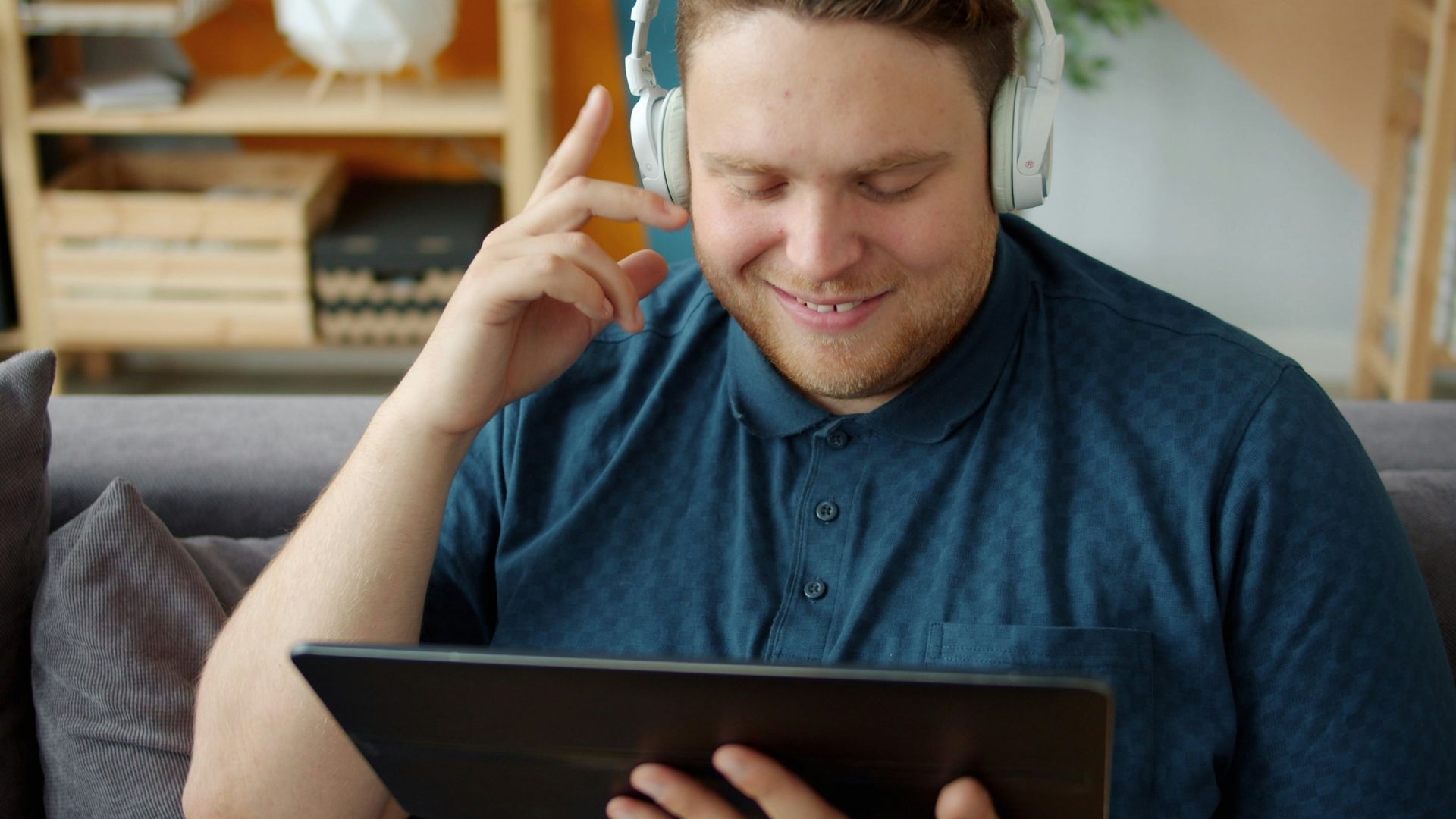 Man wearing headphones watches a tablet on couch.
