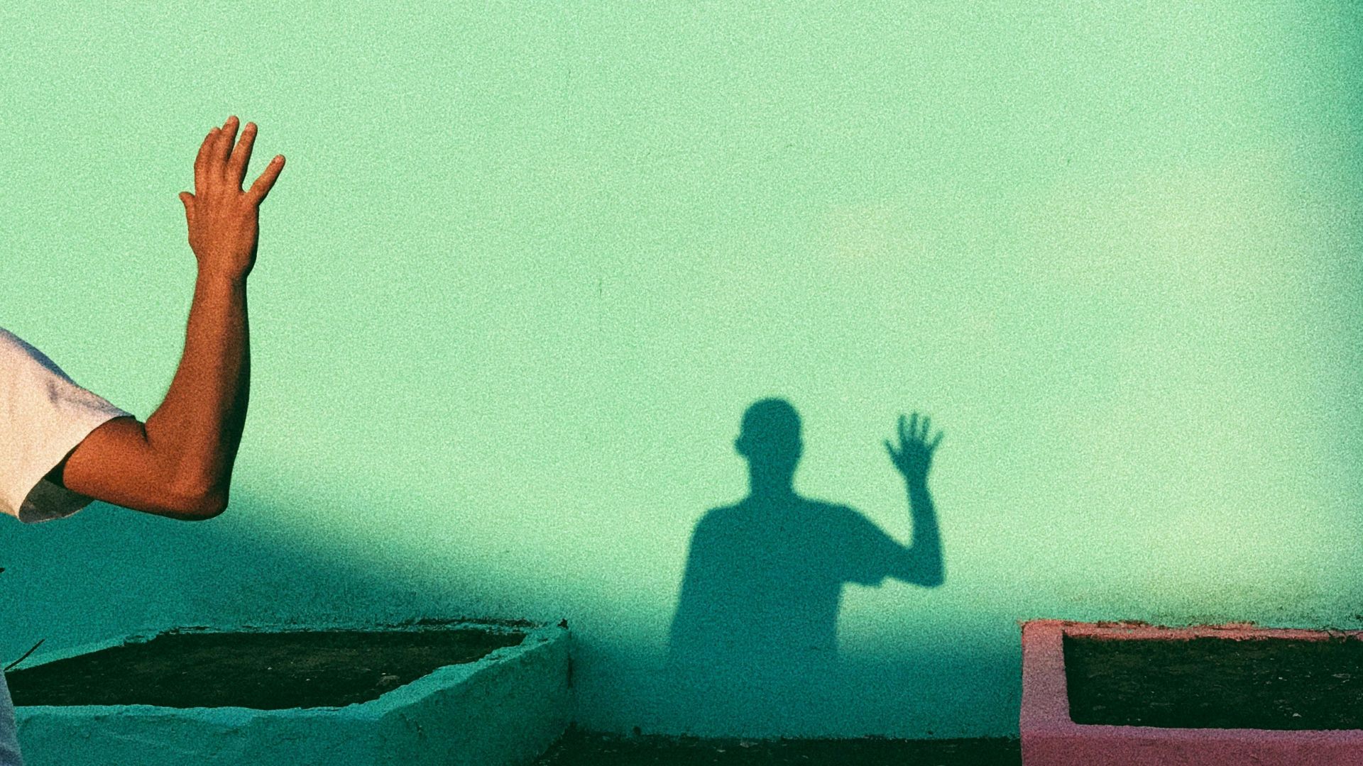 person waving reflecting shadow on teal wall paint