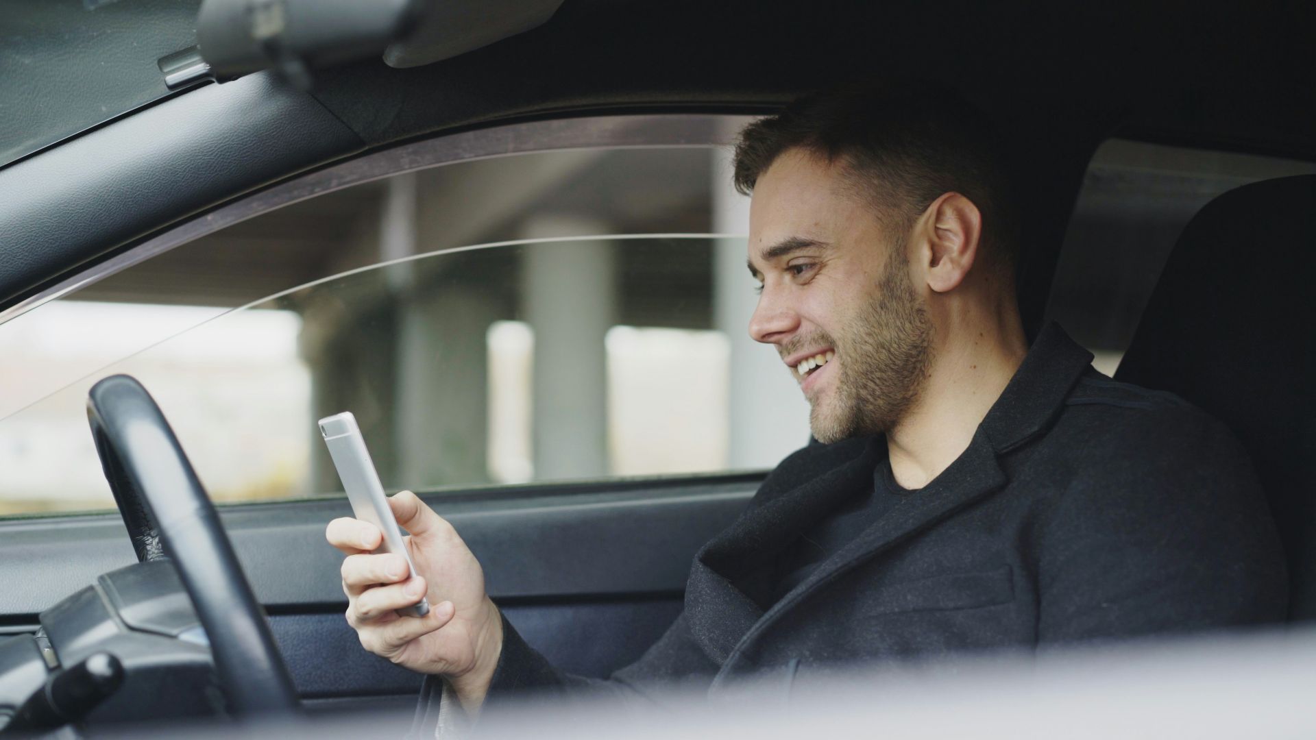 Man smiling while looking at his phone in car