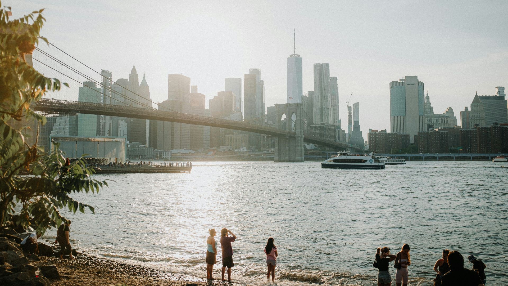 a group of people standing on a rocky shore by a body of water with a bridge and a
