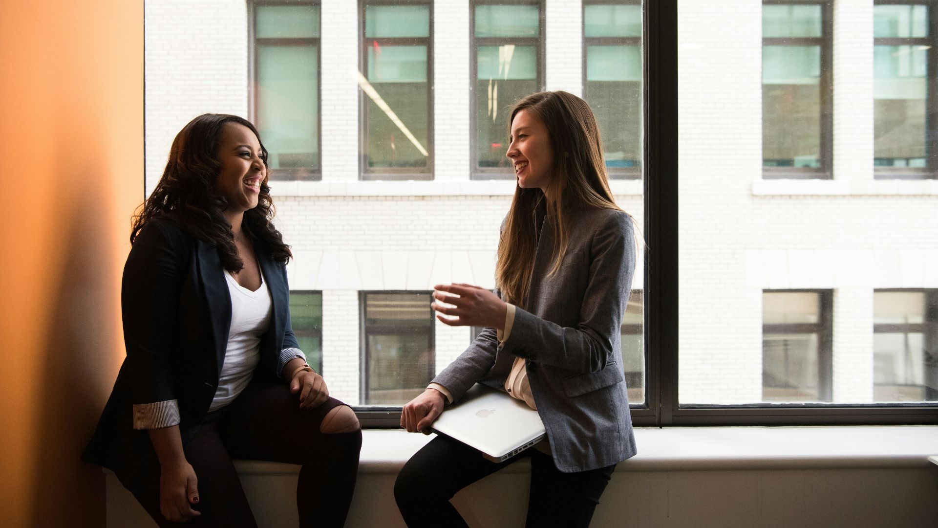 two woman sitting by the window laughing