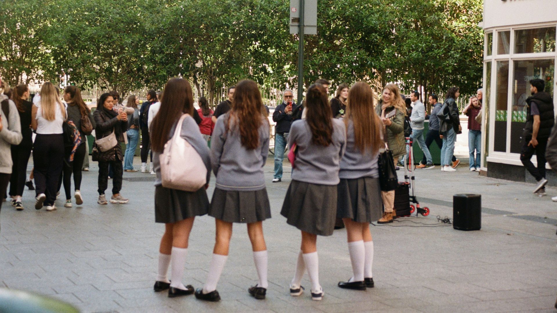 Four girls in school uniforms stand together outside.