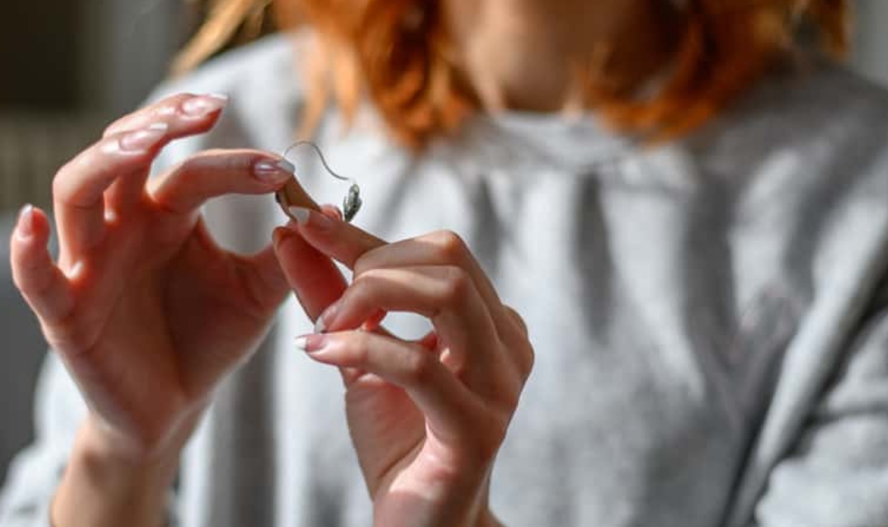 Young Redhead Woman Holding Hearing Aid, Shutterstock, 1976669993