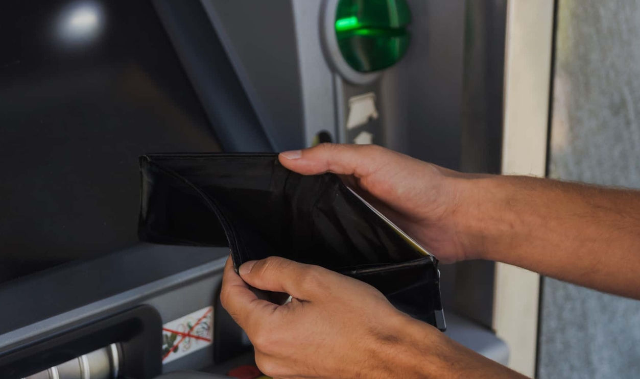 Man Holding Empty Wallet Near Atm Machine - Gettyimages-1044947062