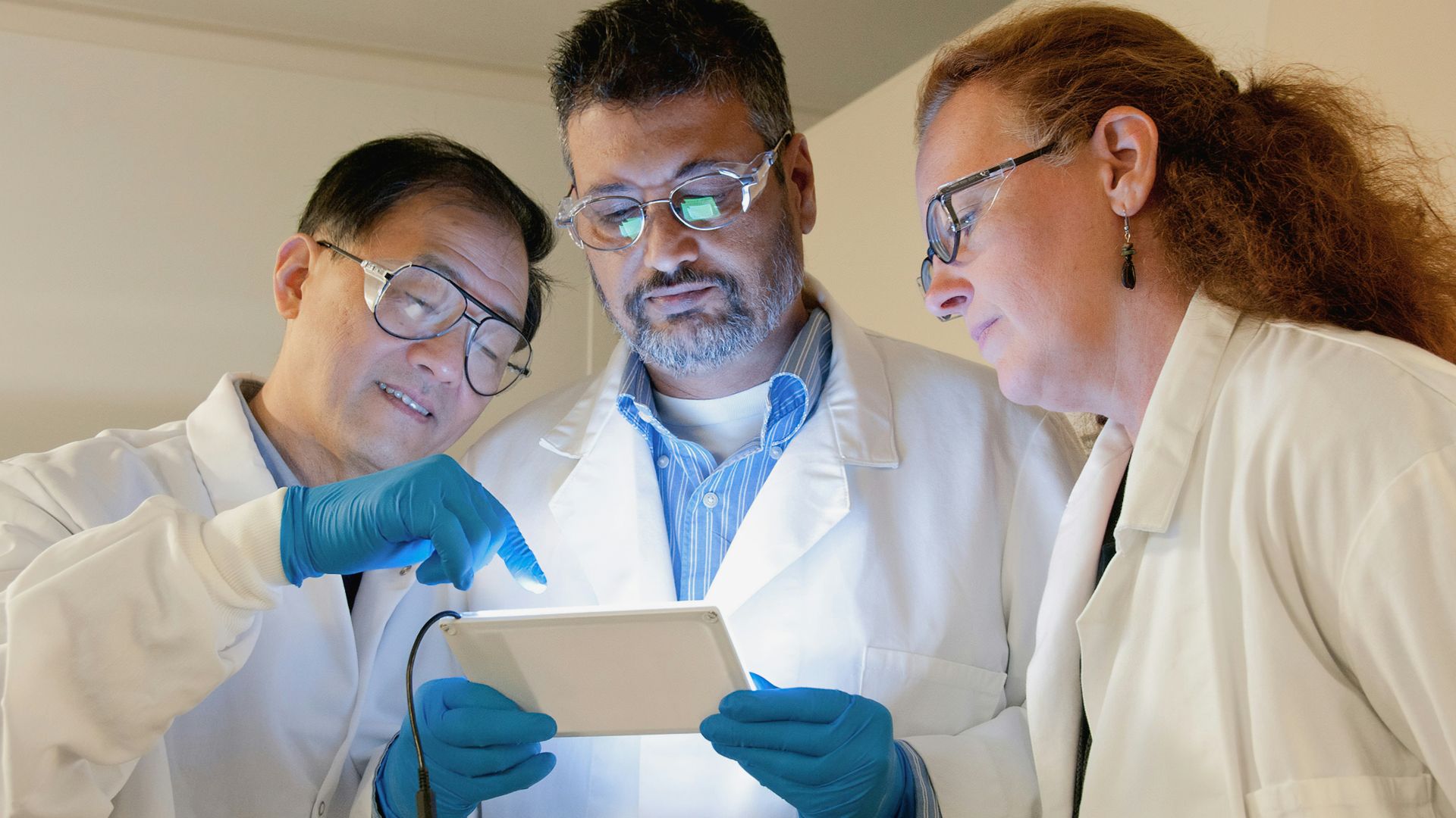 three people in lab coats looking at a tablet
