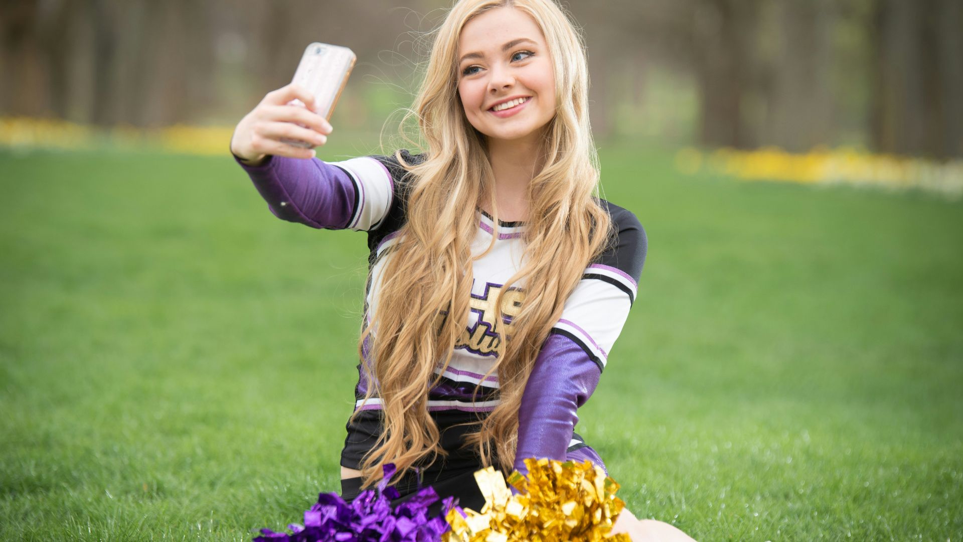 a girl sitting on the grass taking a selfie with her cell phone