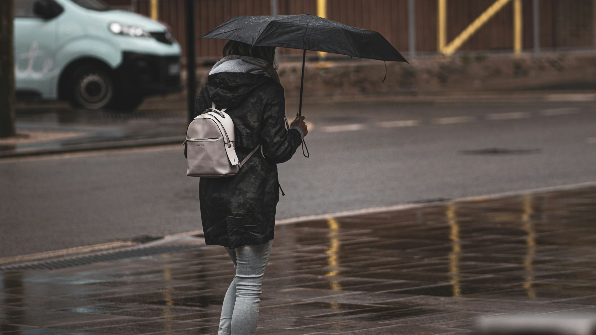 person in black jacket and black pants holding umbrella walking on sidewalk during daytime