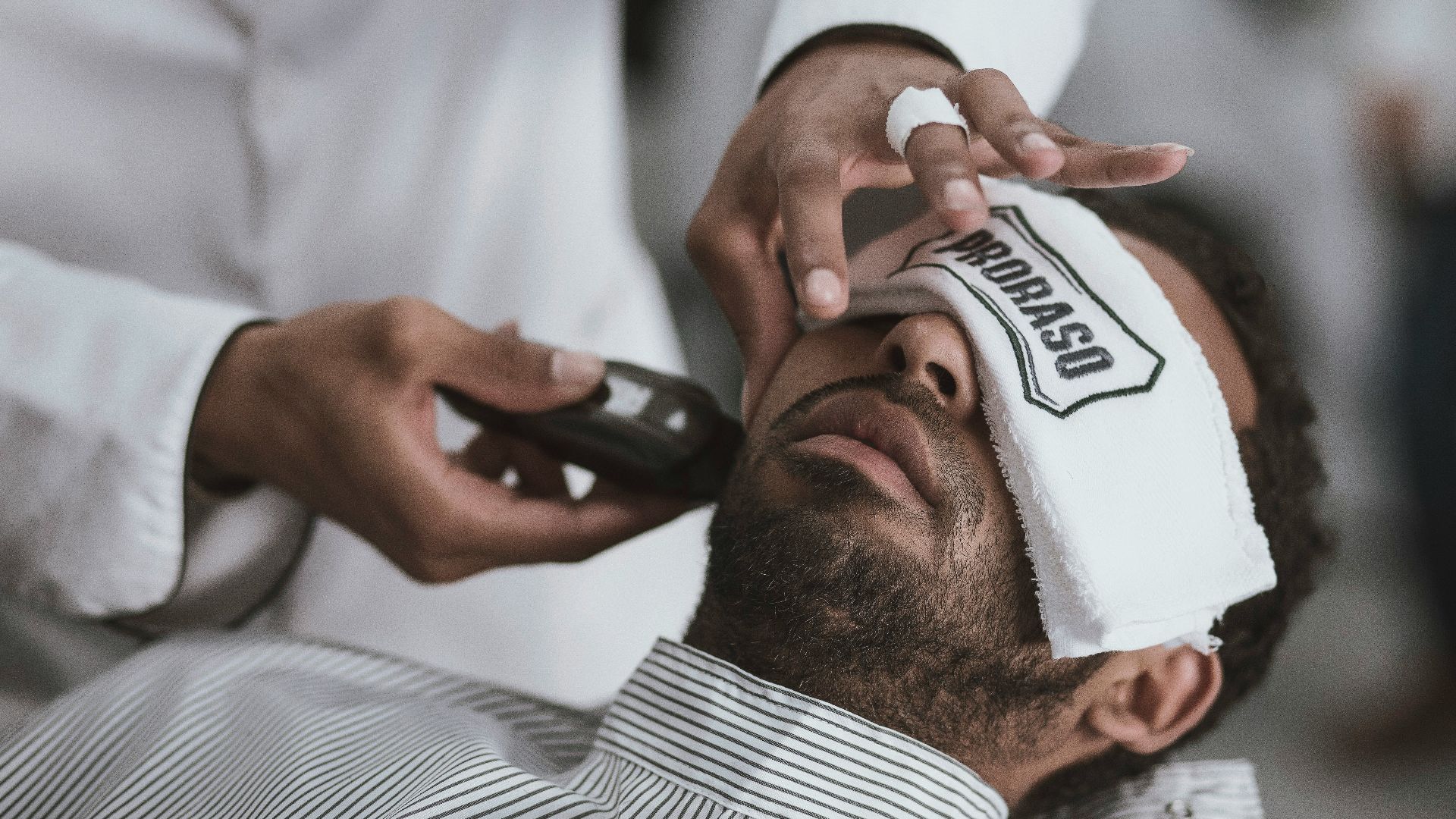 man shaving lying man