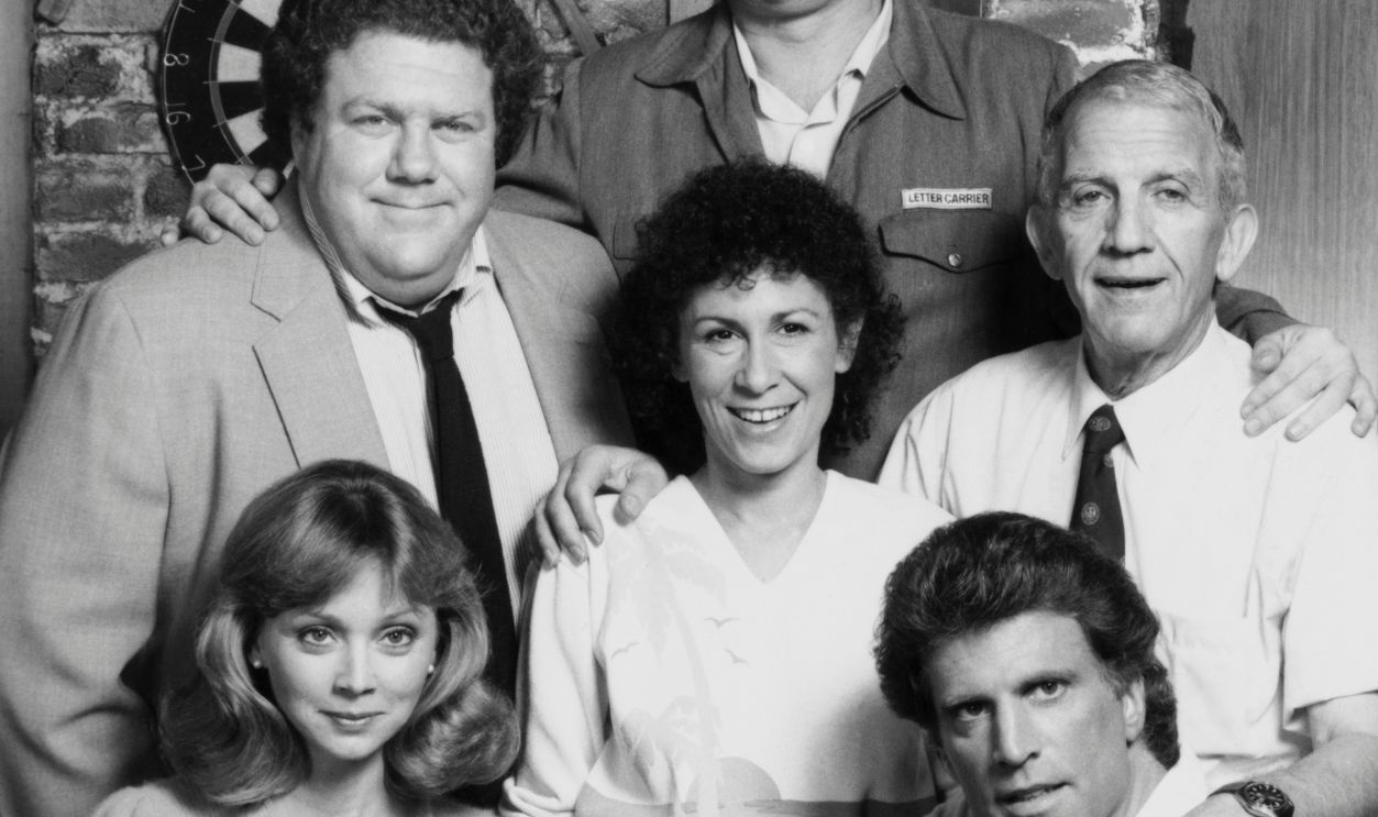 The cast of Cheers pose together in character. From left to right starting with the front row are: Shelly Long, as bartender Diane Chambers; Ted Danson, as bartender and owner Sam