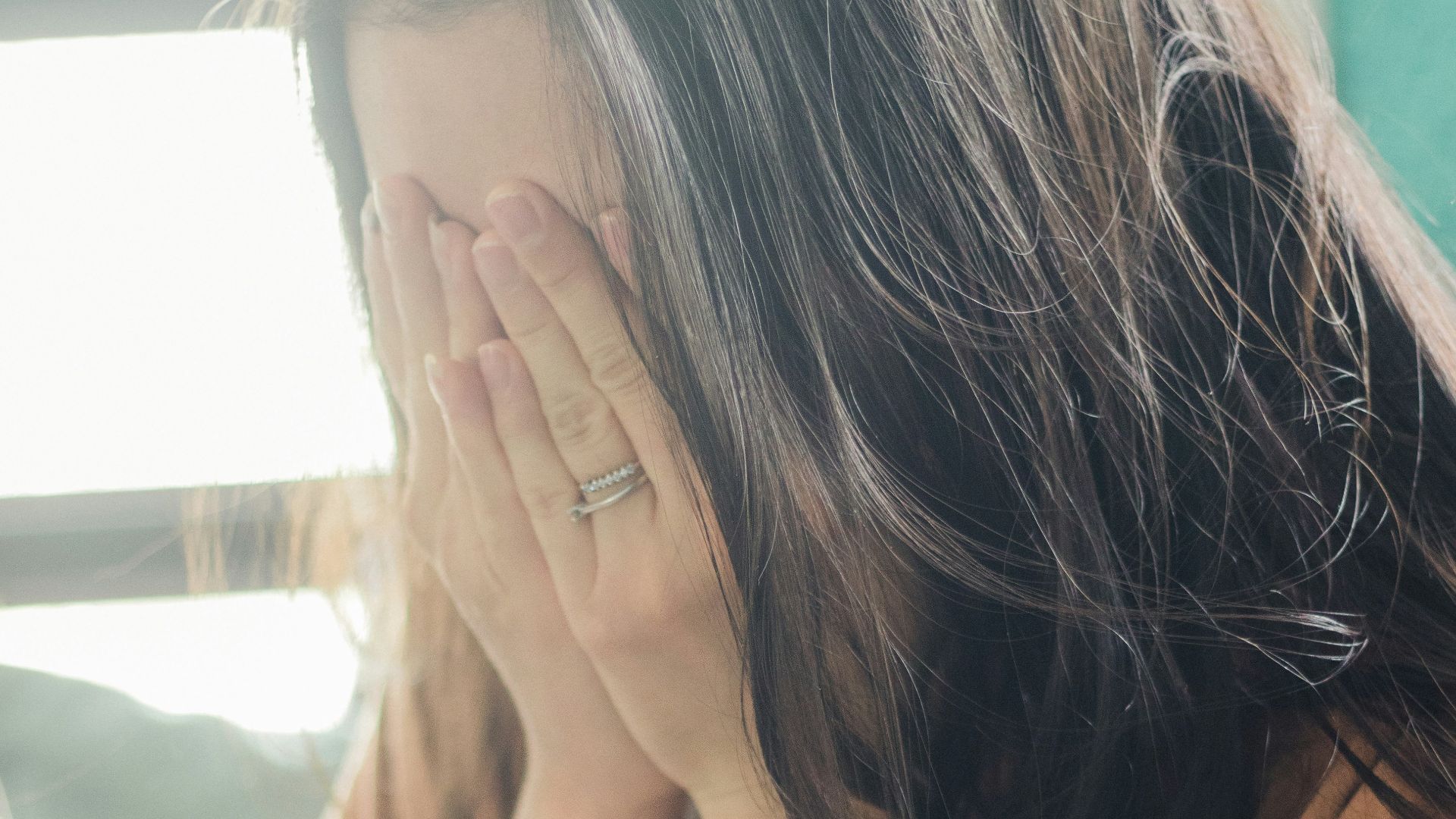 woman in brown shirt covering her face