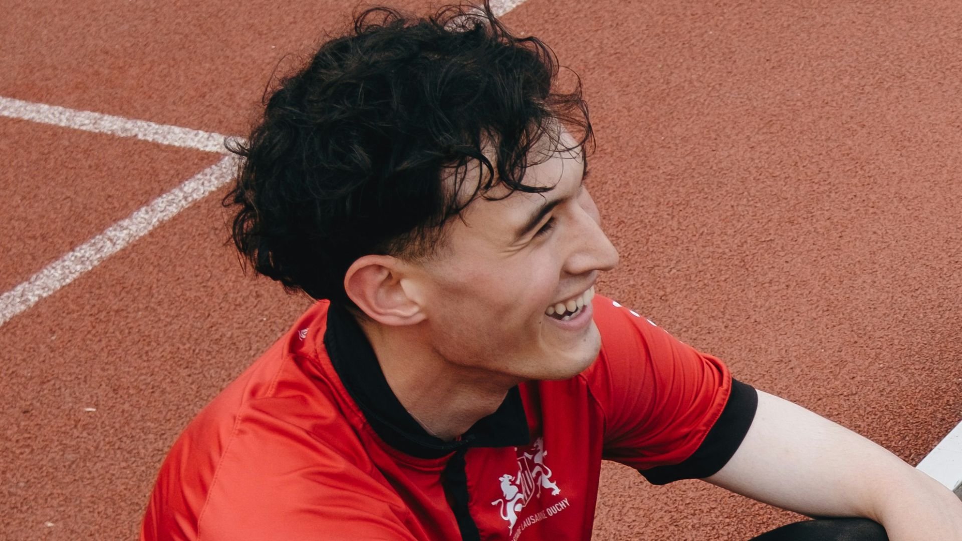 A young man sits on a track, smiling.