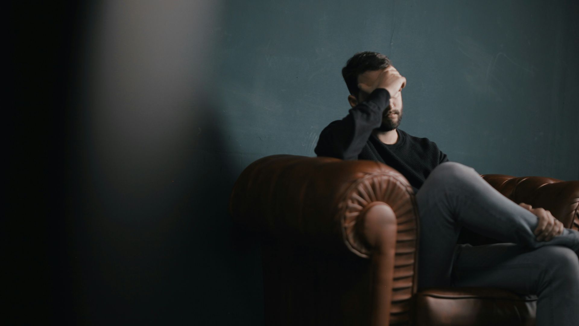 a man holds his head while sitting on a sofa