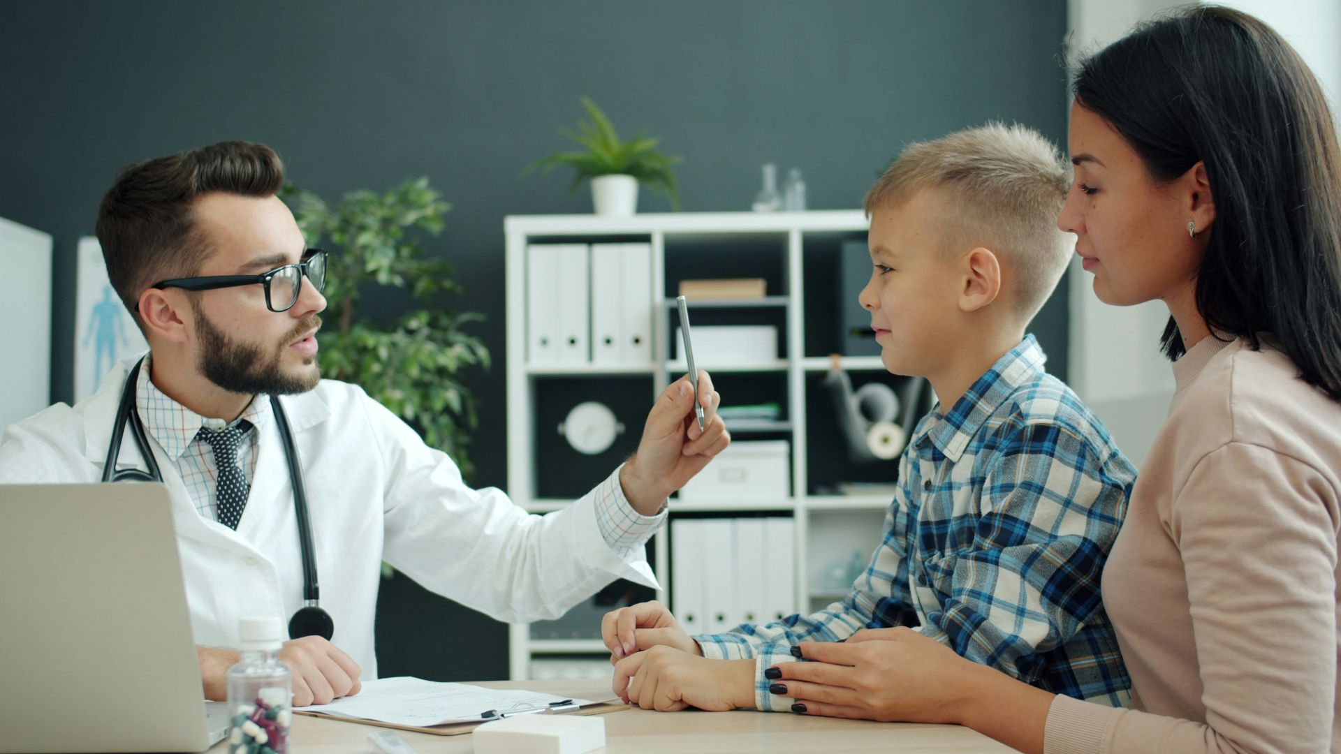 Doctor examines a young boy with his mother present.