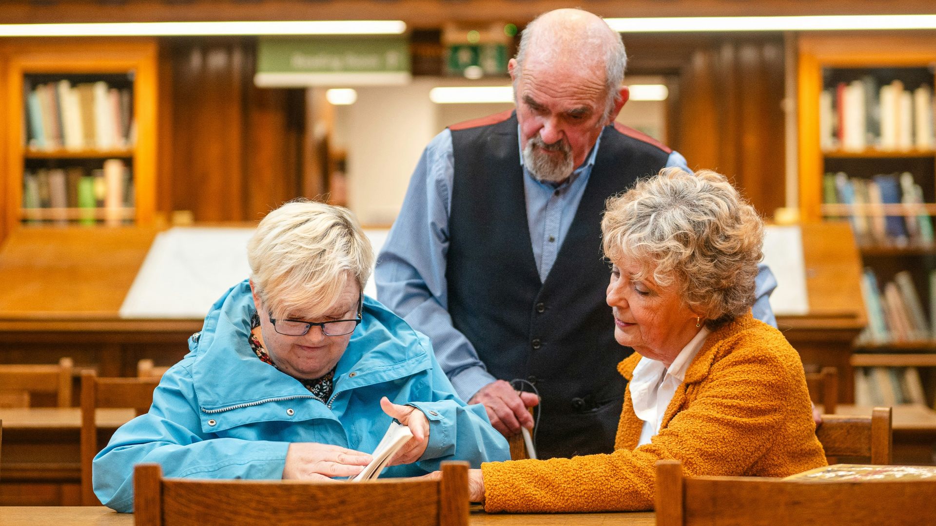 Three people gathered at a wooden table in library.