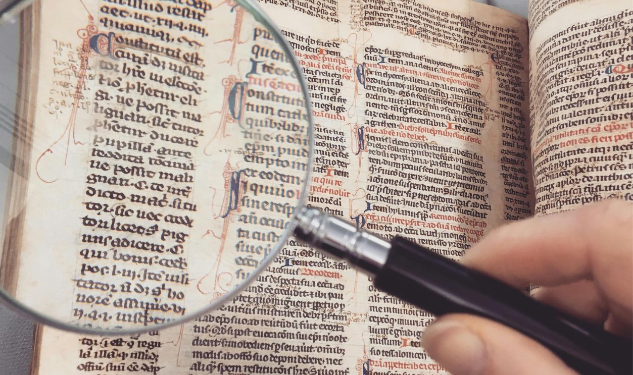 Person Holding Magnifying Glass Pointing on Book
