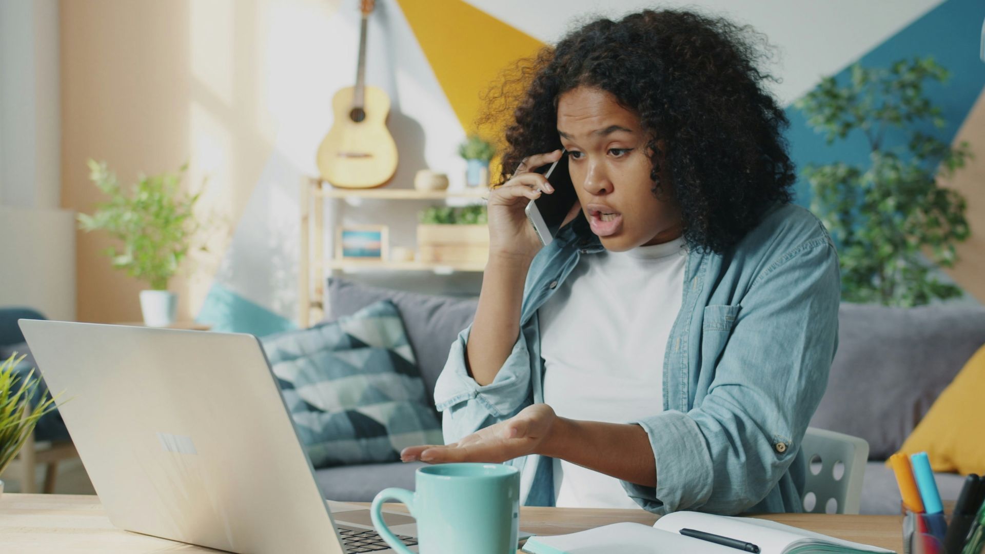 Young woman talking on phone at laptop desk.
