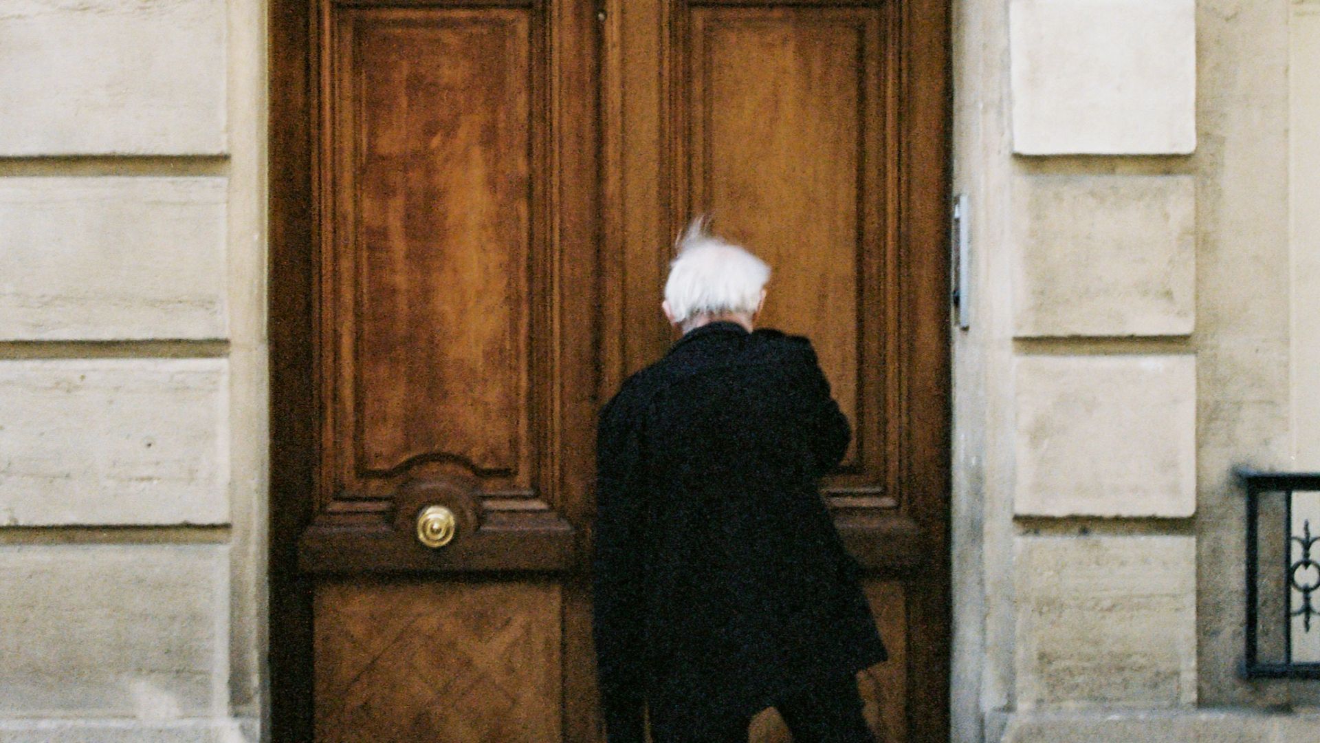 man in black coat standing beside brown wooden door