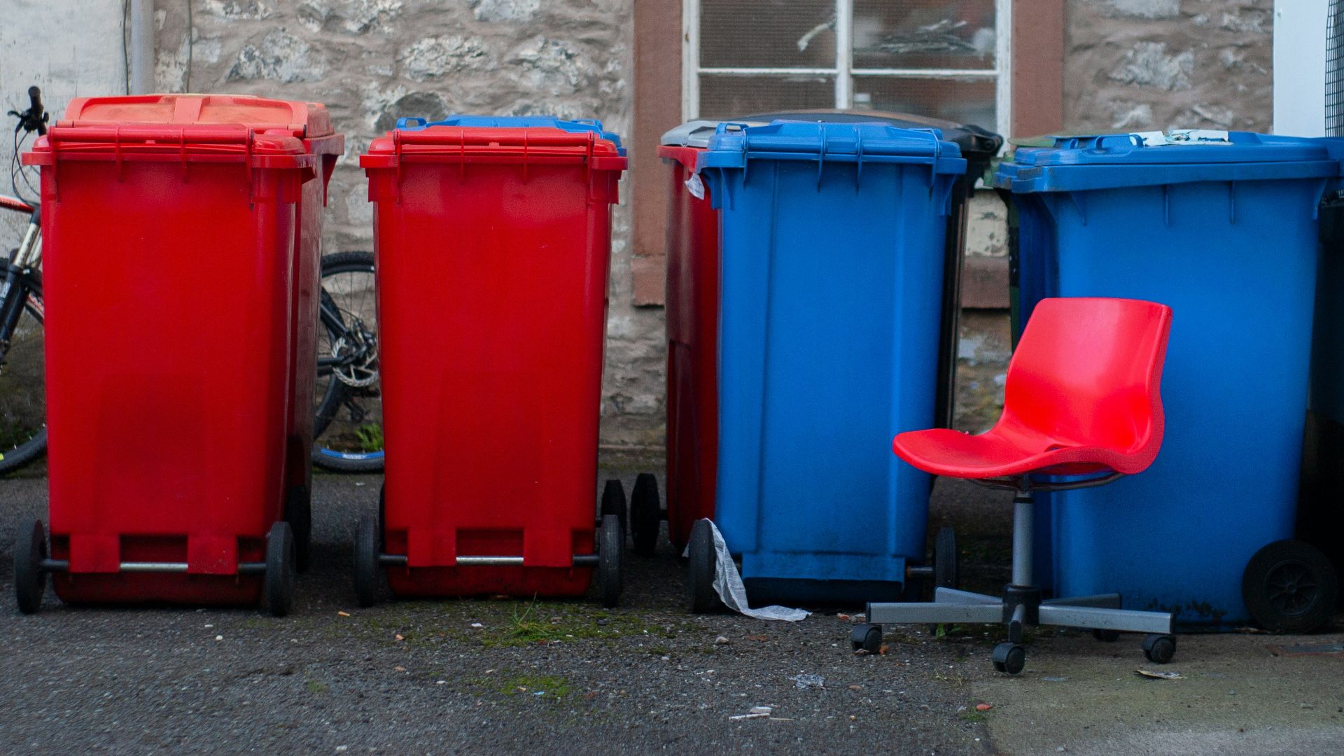 Four colorful trash bins with a red chair.
