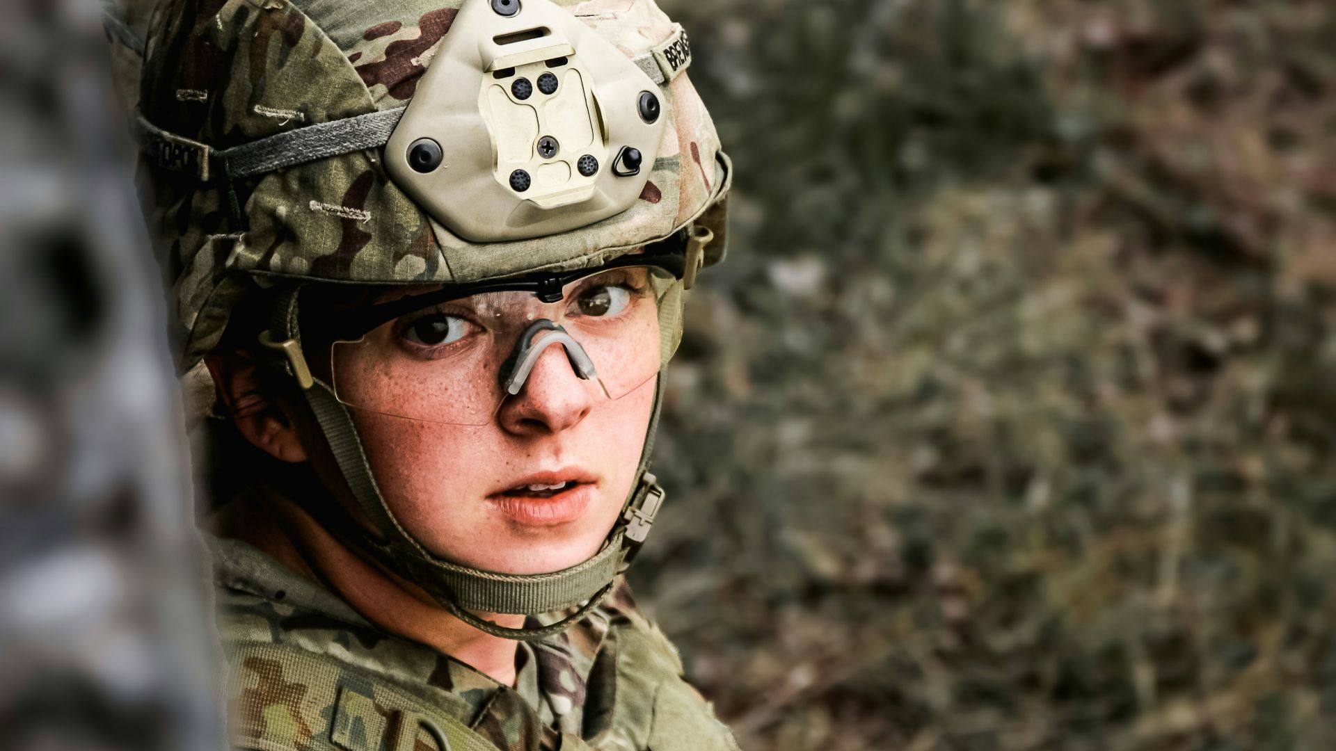 Soldier in camouflage peeking from behind a tree