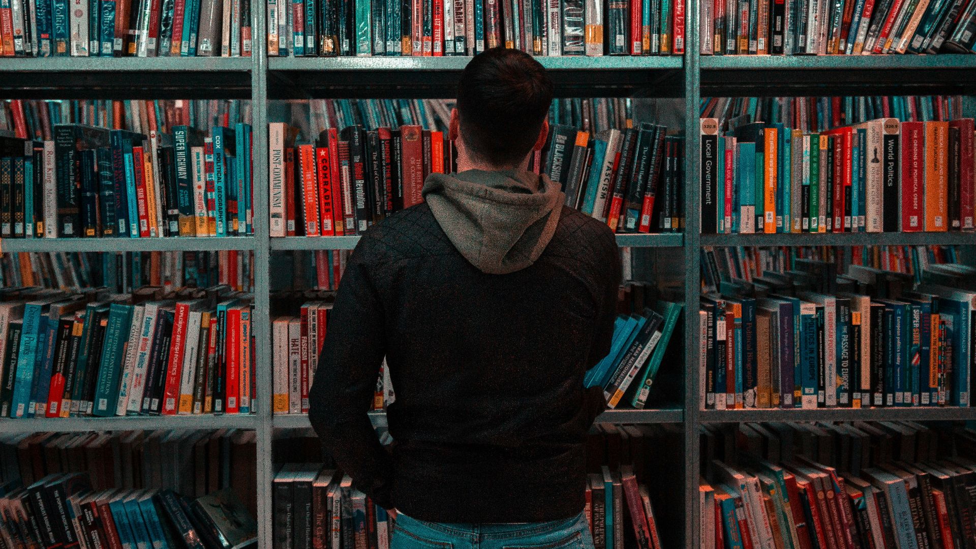 person wearing black and gray jacket in front of bookshelf