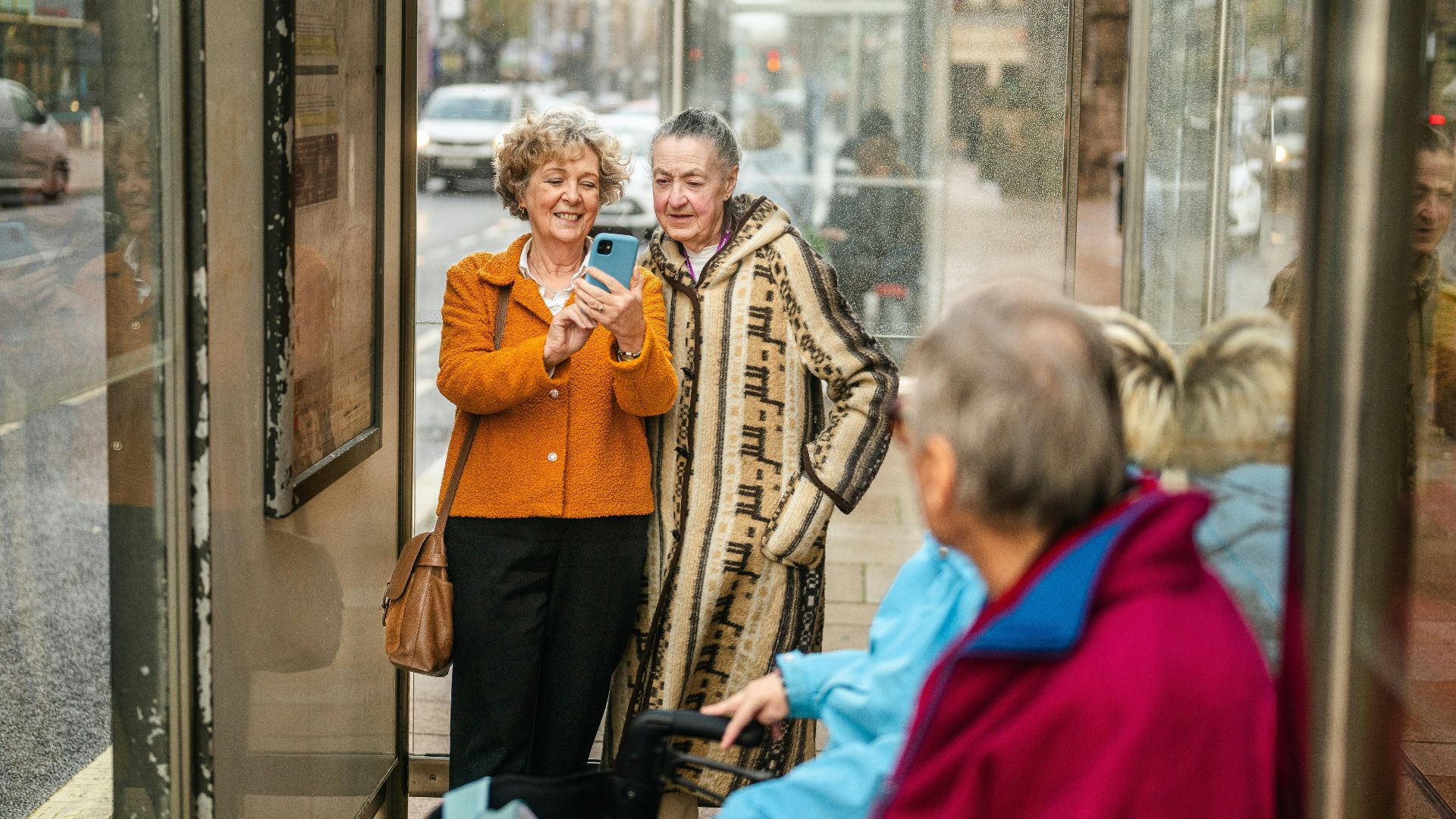 Two women looking at a smartphone at a bus stop.