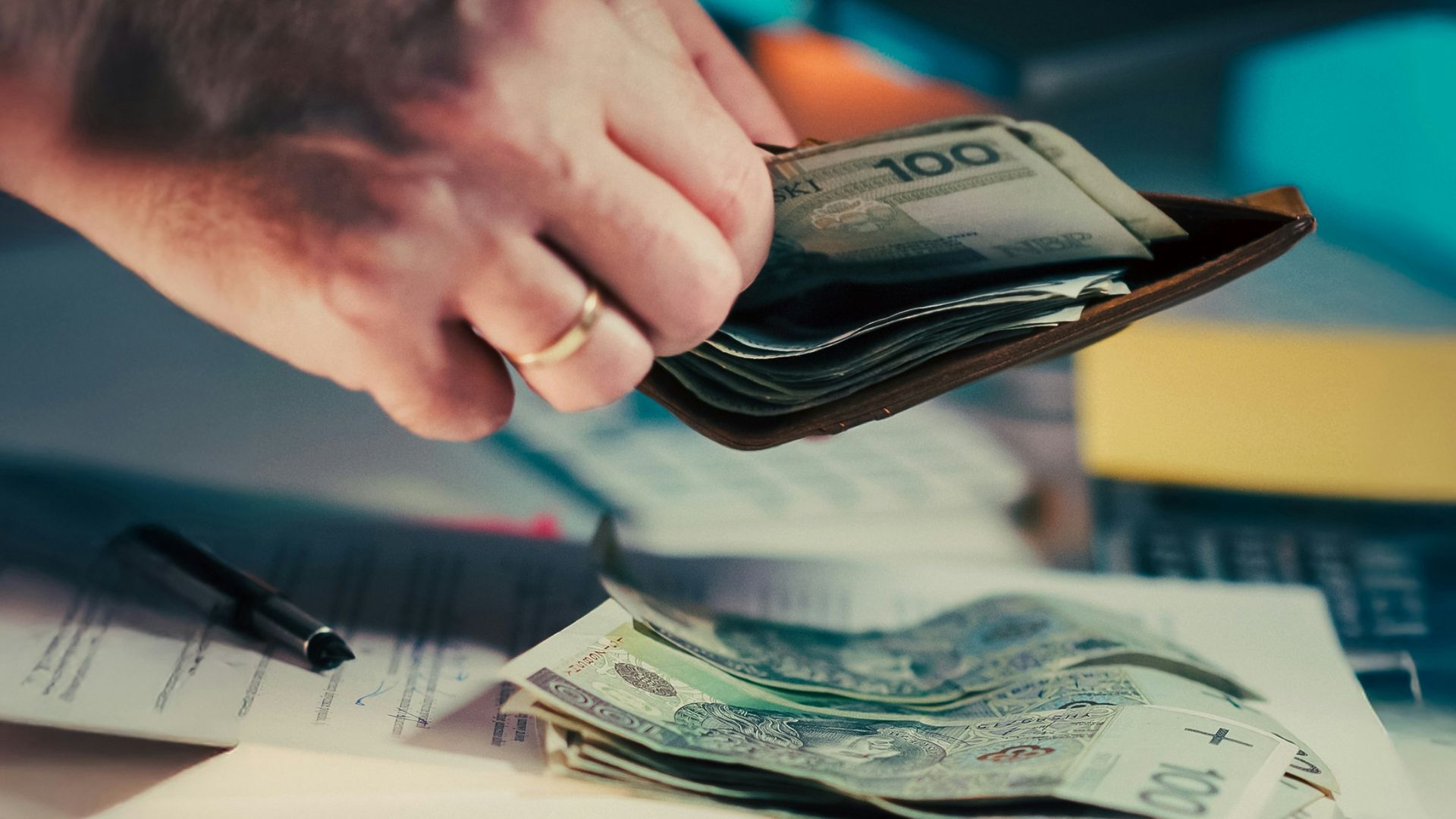 Hands counting money from a wallet over papers.