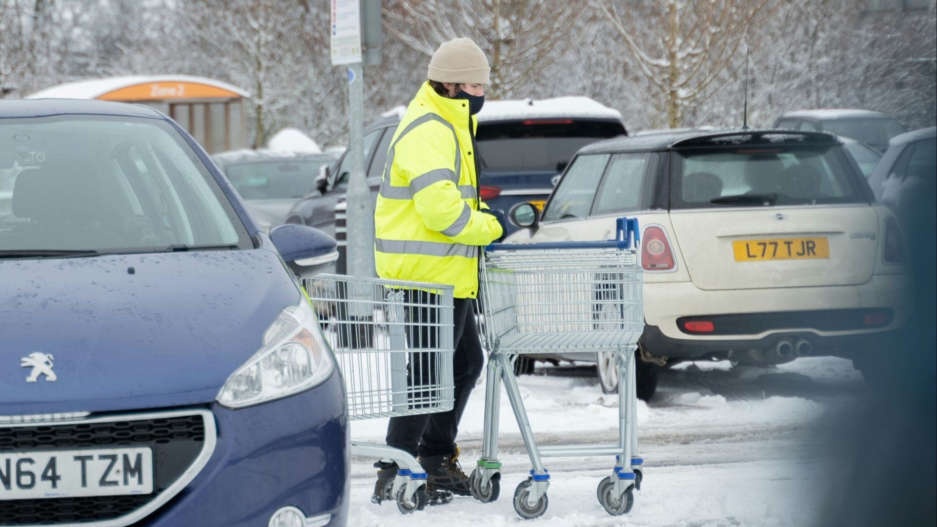man in yellow jacket and white knit cap standing beside blue honda car during daytime