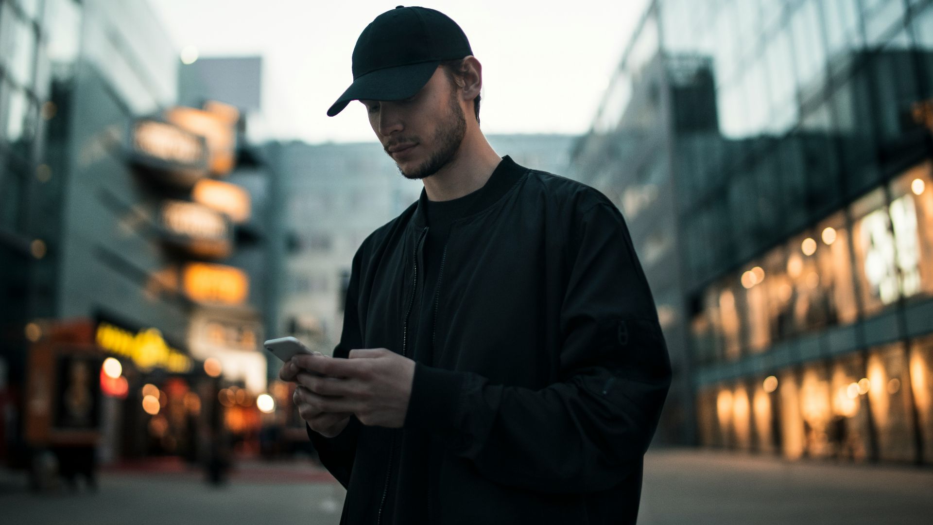 man in black jacket wearing black fitted cap while using phone