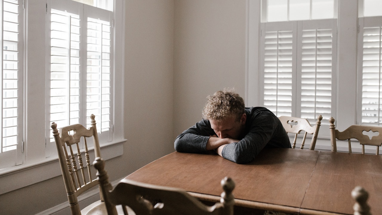 Sad man is sitting on wooden chair in dinning room.