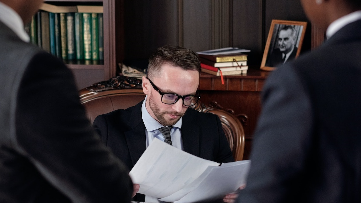 Two lawyers are standing in front of a judge seating on the desk.