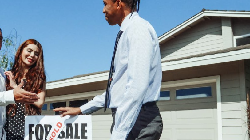 The image shows three individuals standing in front of a house with a "FOR SALE"