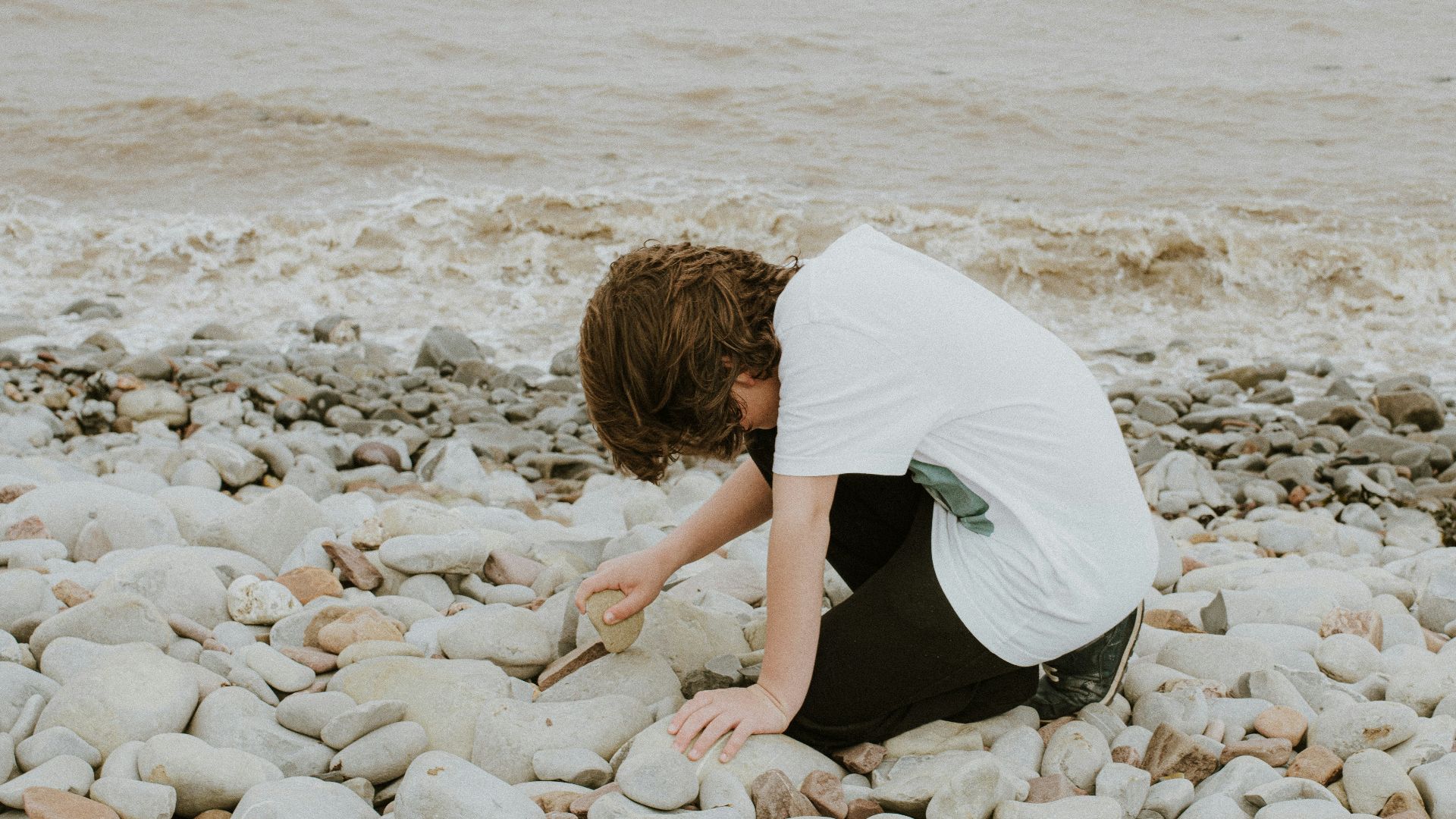 a person kneeling down on a rocky beach