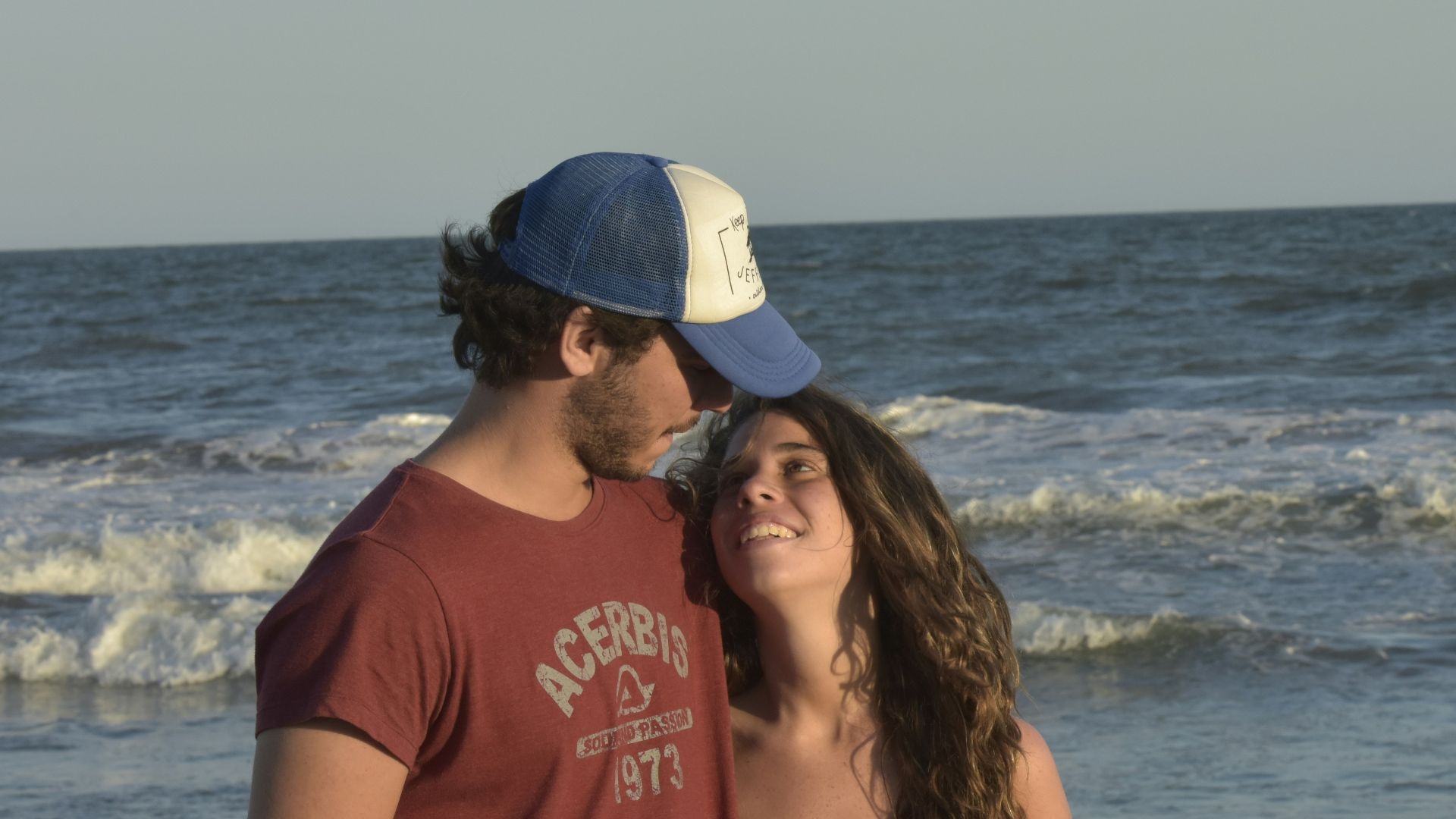 woman in red shirt and blue denim daisy dukes standing on beach shore during daytime