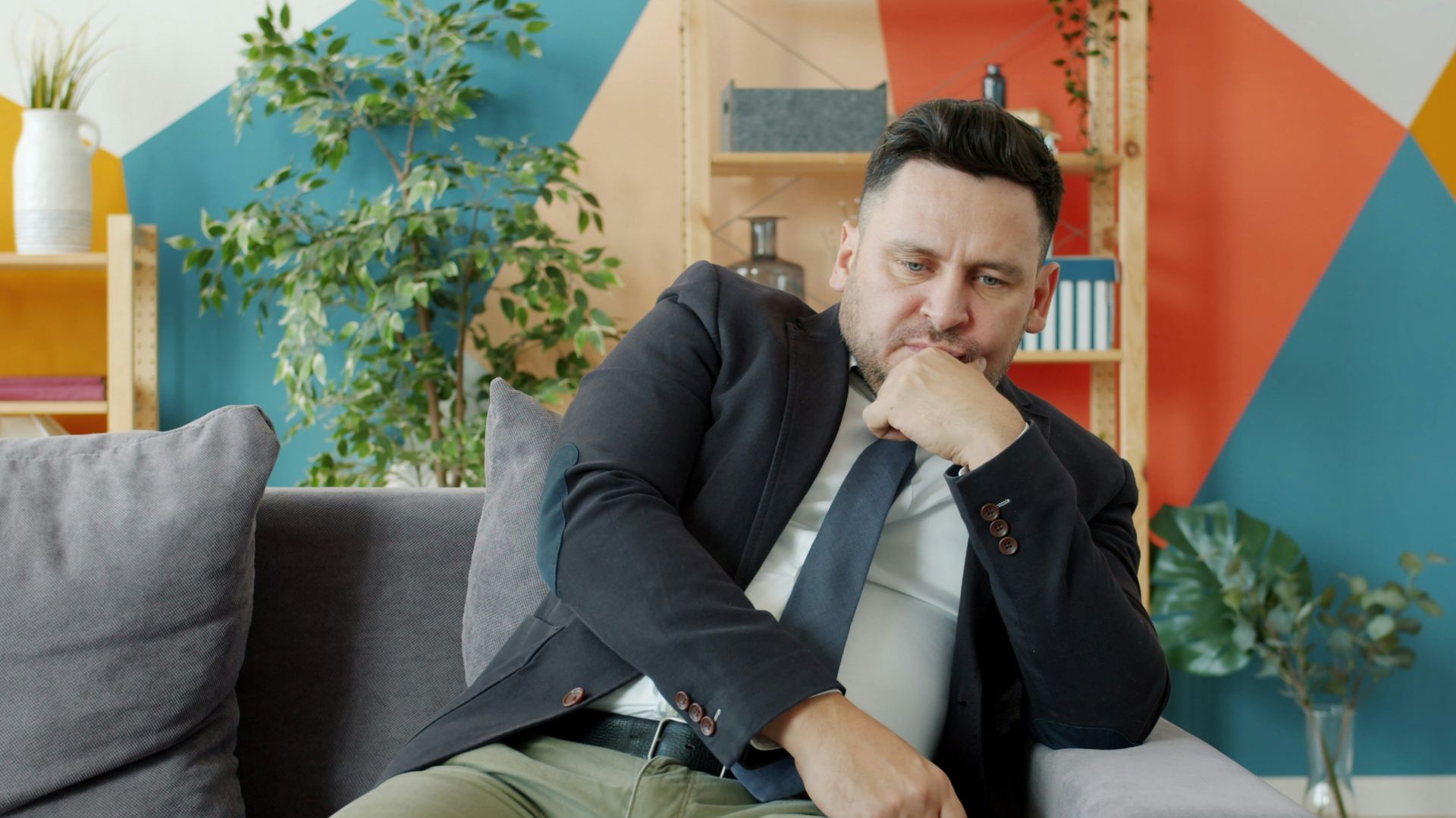 Man in suit sitting on couch looking thoughtful.