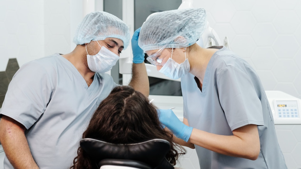 Woman seating on dentist chair with two dentists by her side.
