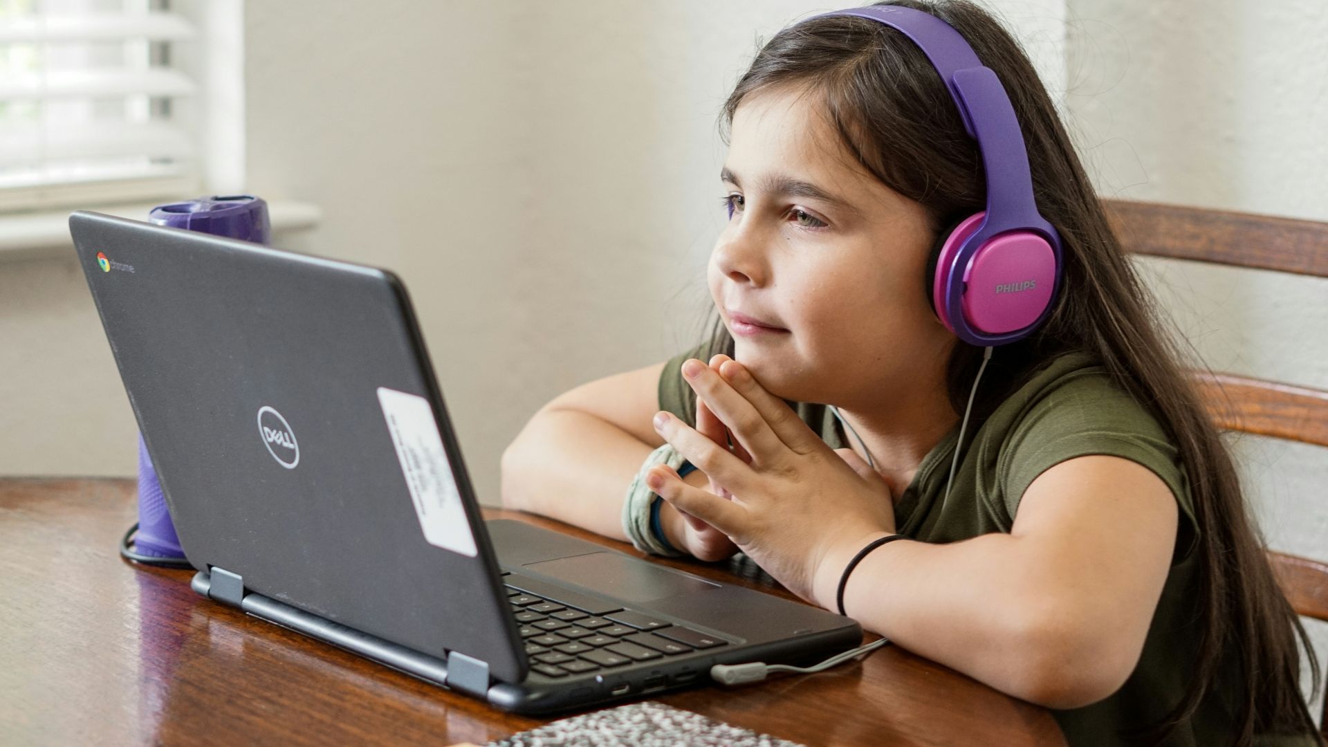 a little girl sitting at a table with a laptop