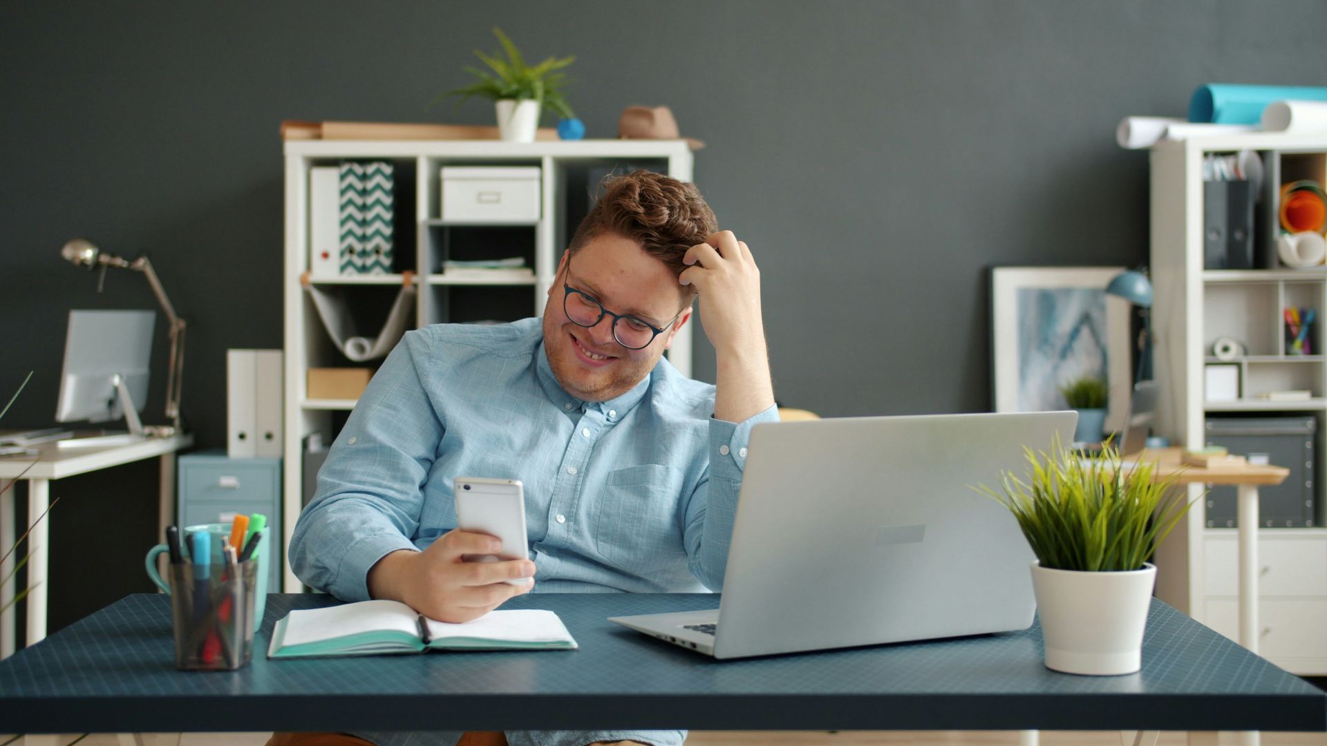 Man laughing while looking at his phone at desk.