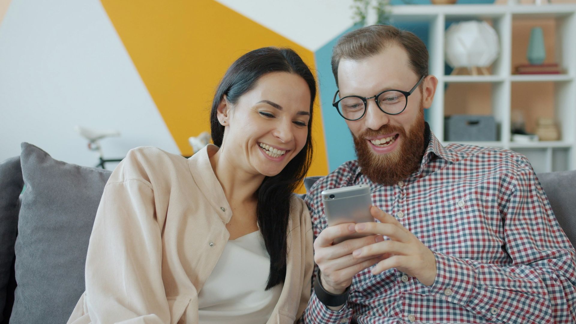 Couple laughing while looking at a smartphone together.