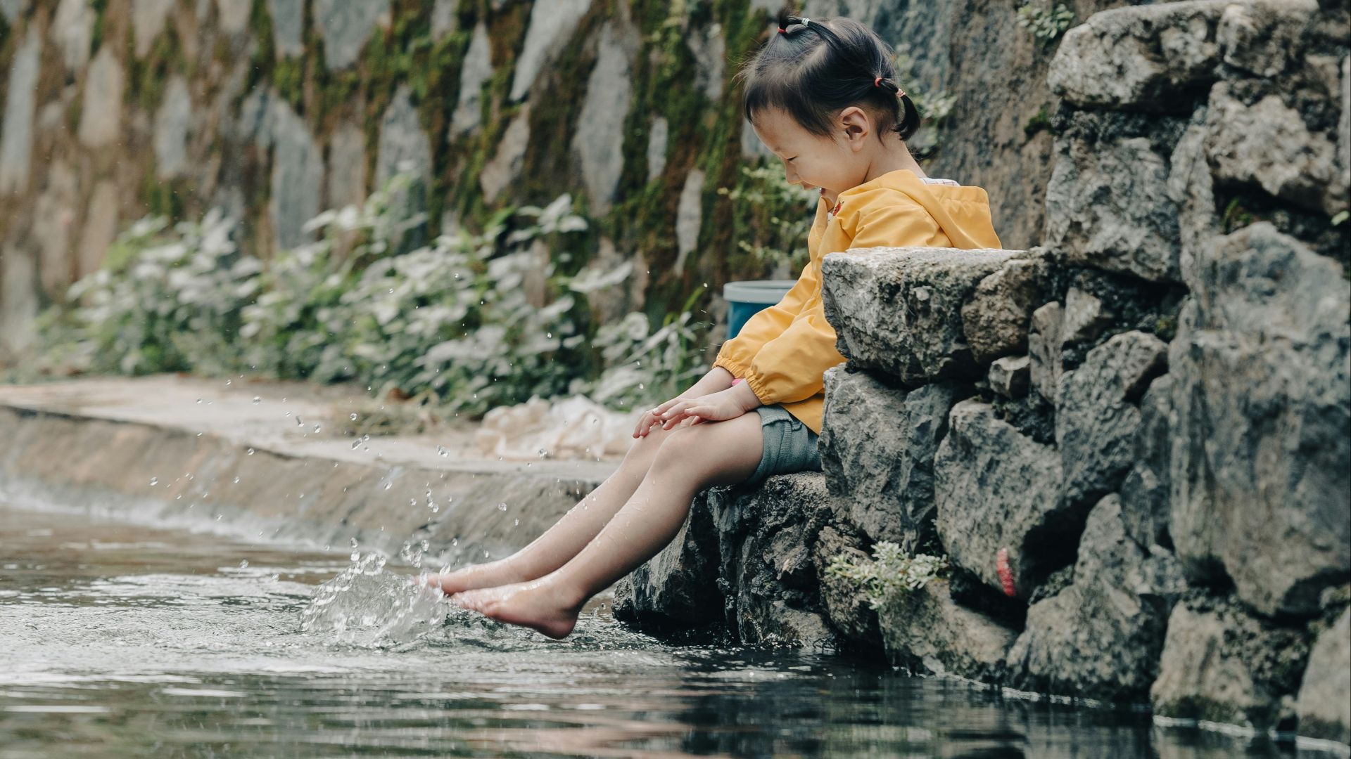 a young boy sitting on a rock next to a body of water