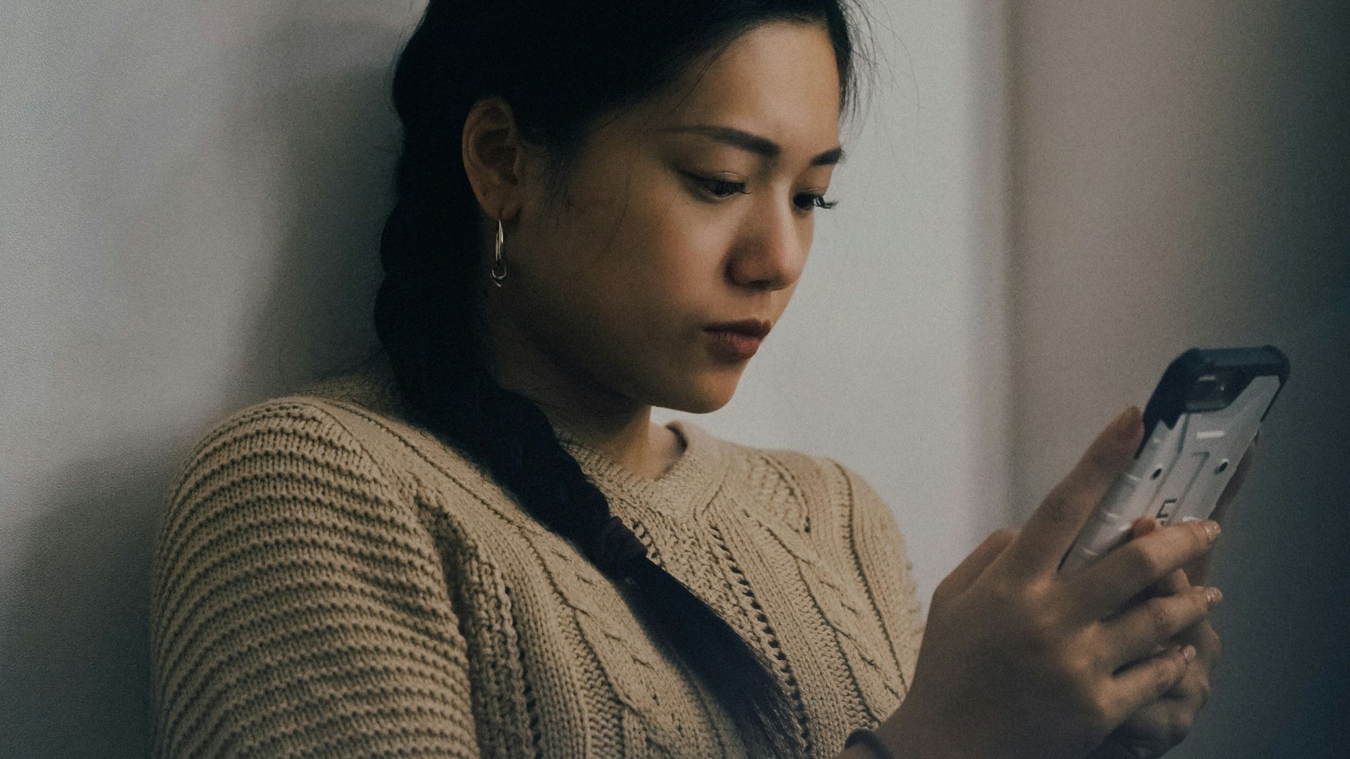 woman leaning back on white wall and using smartphone