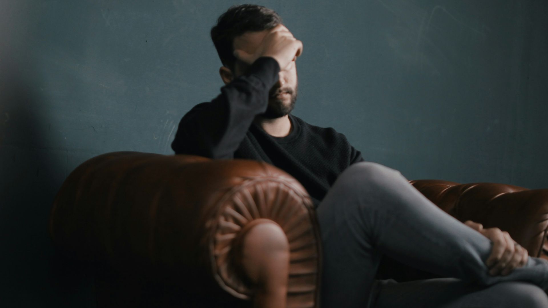 a man holds his head while sitting on a sofa