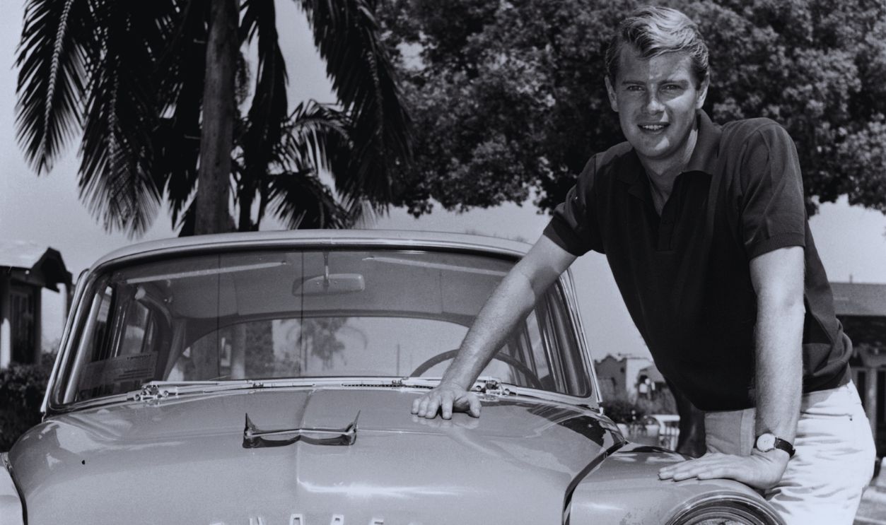 Gettyimages - 3202691, Troy's Toyota 1956: Portrait of American actor Troy Donahue (1936 - 2001) leaning on the hood of a Toyota Toyopet car with a California license plate, in front of a palm tree on a residential street, California. Donahue wears a dark polo shirt and pale colored jeans. 