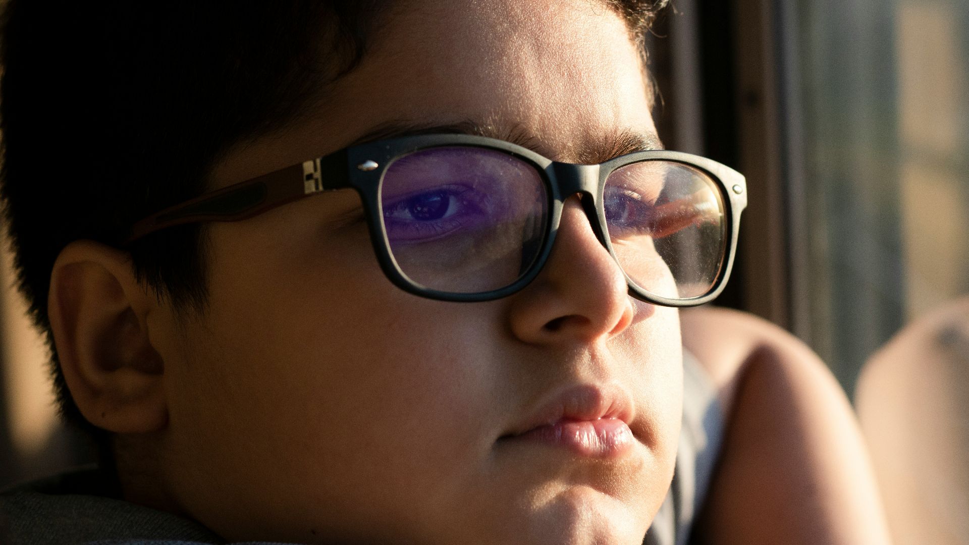 a young boy wearing glasses looking out a window