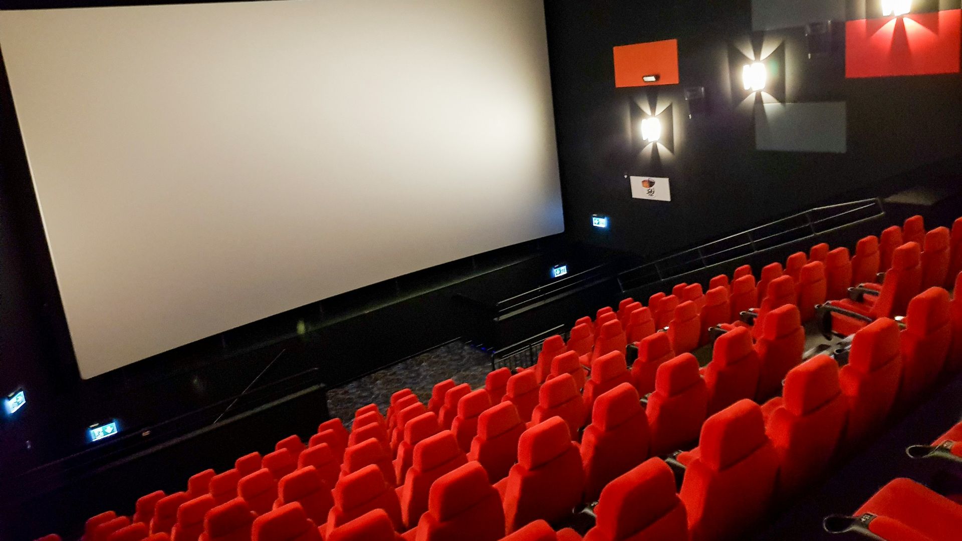 an empty theater with red seats and a projector screen