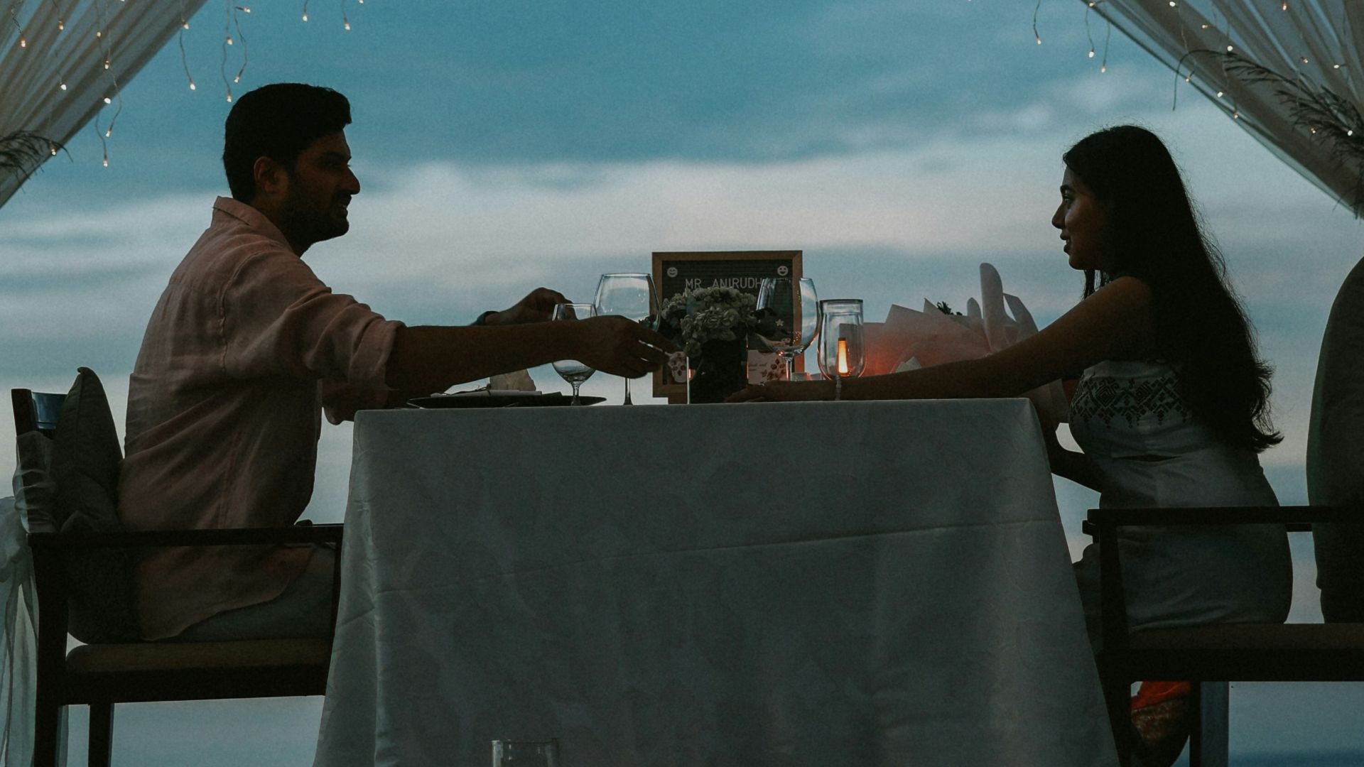 Couple having romantic dinner under palm trees at dusk.