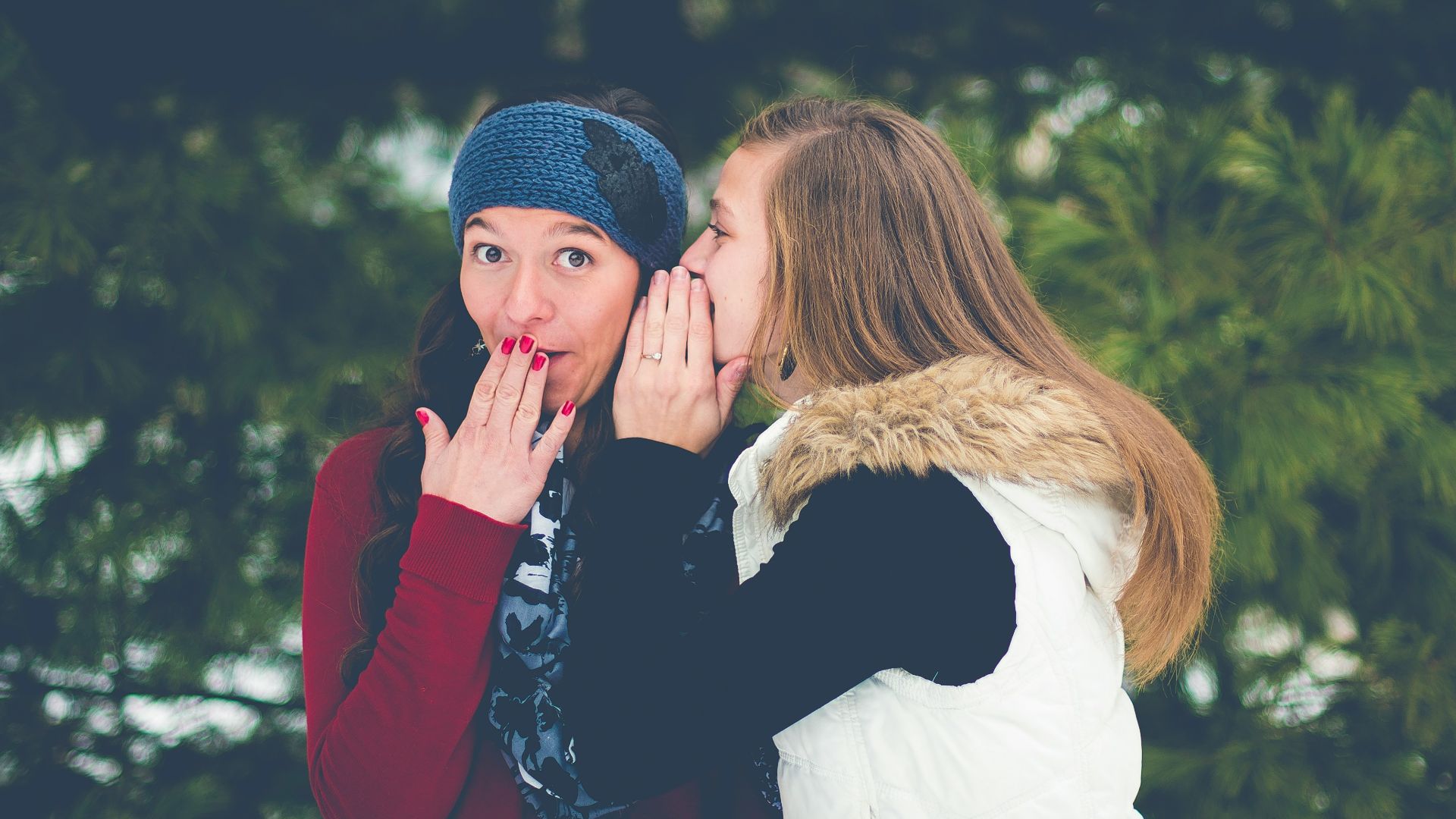 woman whispering on woman's ear while hands on lips