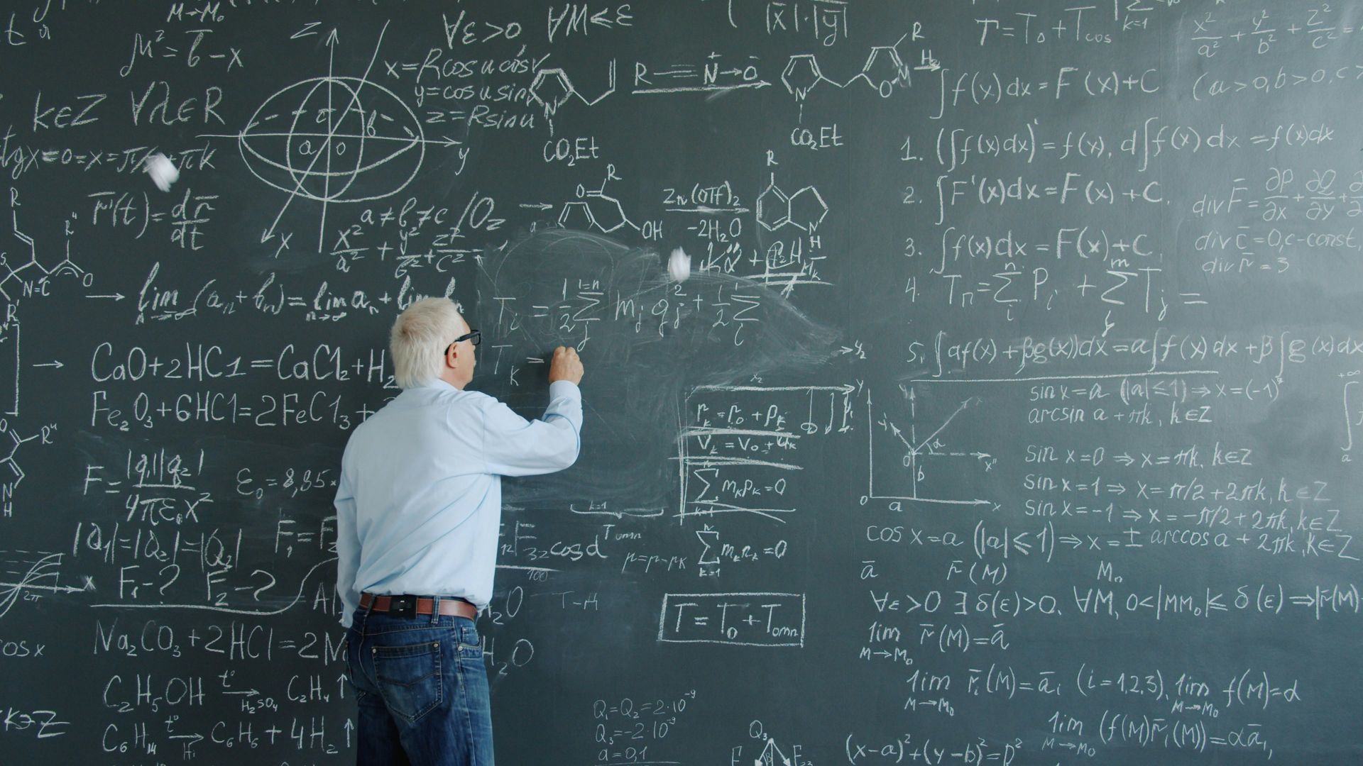 Professor writing complex equations on a blackboard.