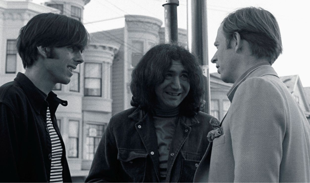 Author Tom Wolfe talks with Jerry Garcia of the Grateful Dead and the band's manager Rock Scully under the street signs on the corner of Ashbury and Haight streets in San Francisco. | Location: corner of Haight and Ashbury streets, San Francisco, California, USA. 
